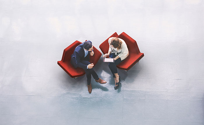 Stylised aerial photo of a man and woman sat on red armchairs looking at a tablet.
