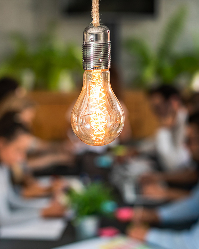 Lightbulb hanging in foreground with blurred image of a people meeting in the background
