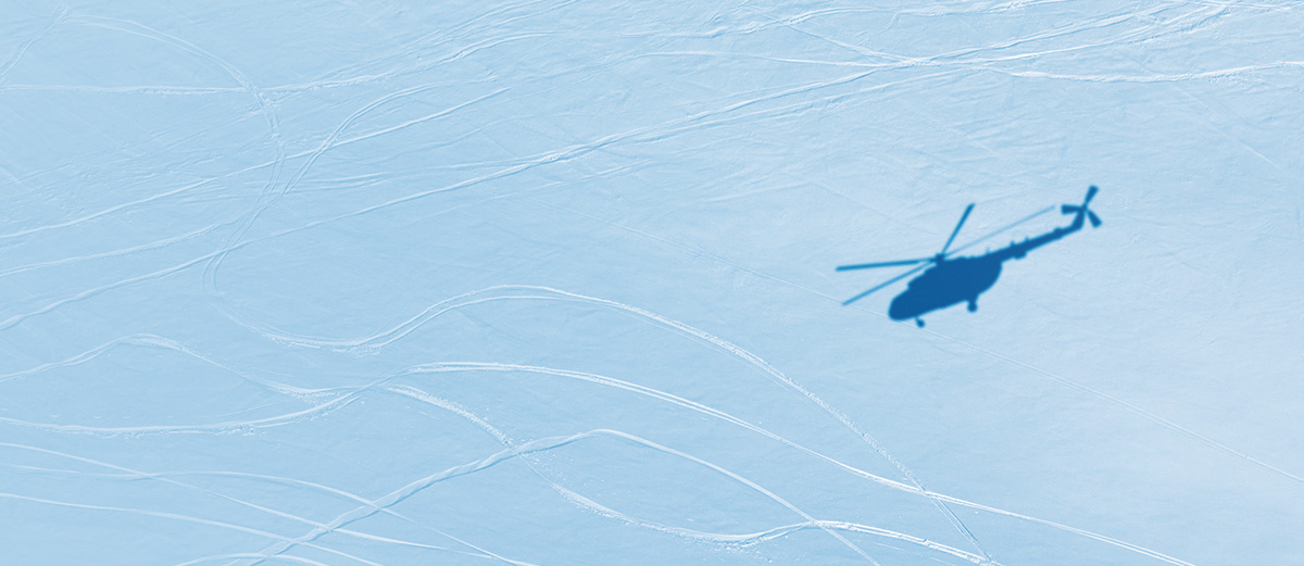The shadow of a helicopter on a snowy mountain with ski tracks