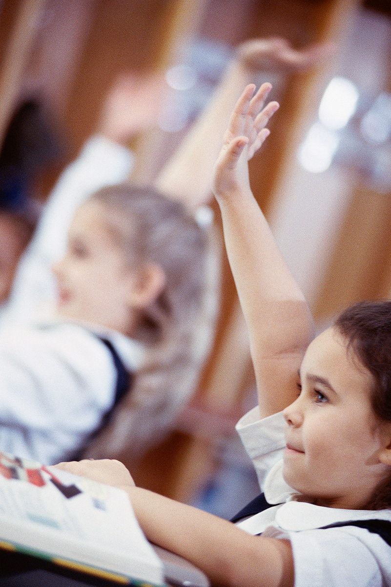 Schoolchildren with their hands up in a classroom.