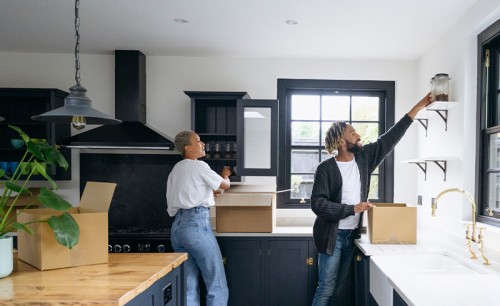 Full length view of mid adult man and woman in casual clothing placing glasses in cabinets and jars on shelves on moving day