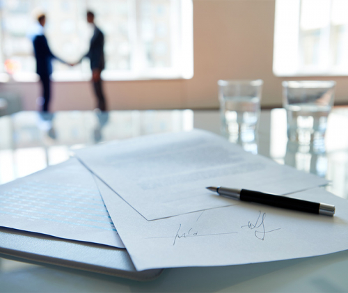 Signed contract lying on table, business partners shaking hands in the background