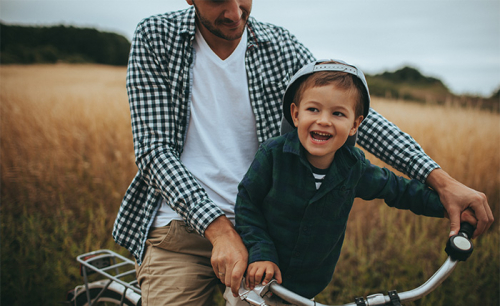 Little boy and his father riding a bicycle outdoors.