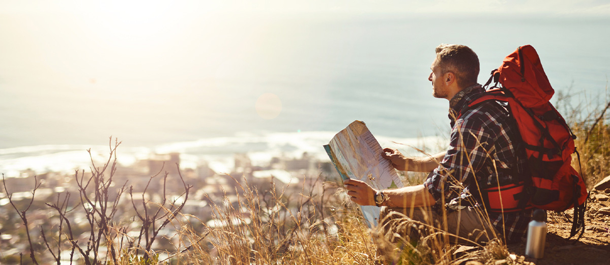 Full length shot of an adventurous male backpacker reading a map while hiking in the mountains