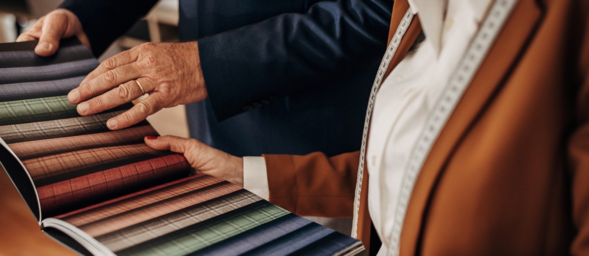 Female tailor showing a catalog with various types of designs to a mature male client for a new suit