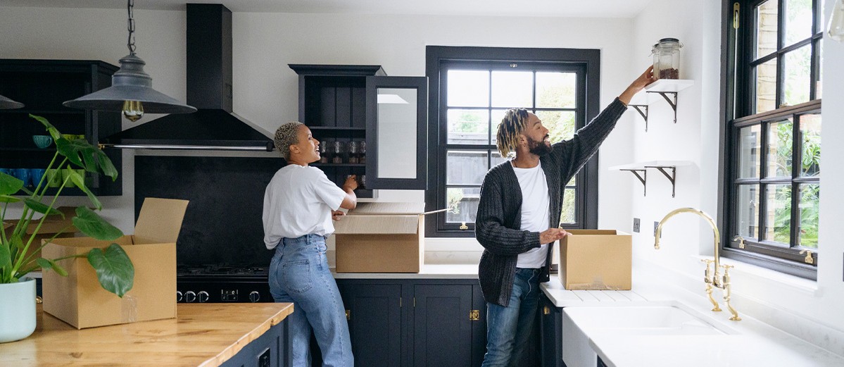 Black couple unpacking boxes in Shaker-style kitchen