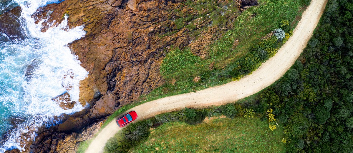 Red car moving on a winding coastal road approaching a beautiful beach