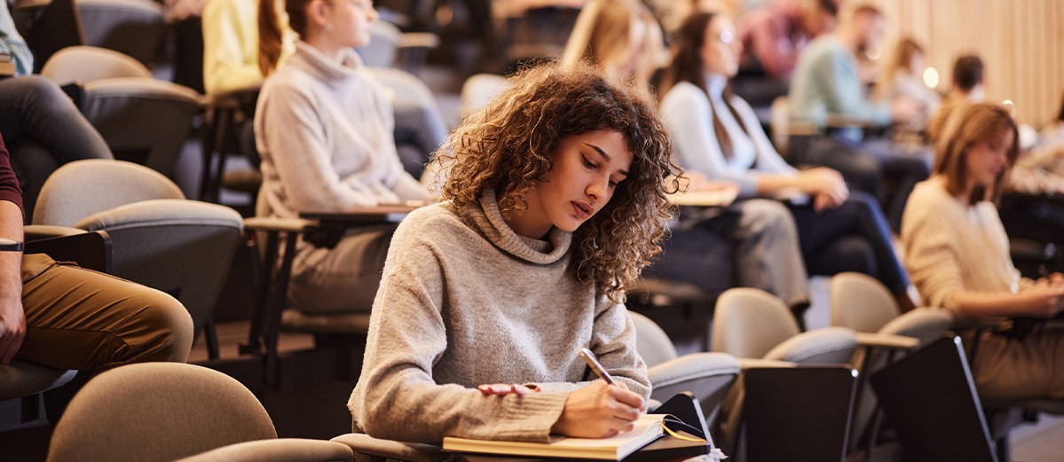 Female college student writing an exam during a class at lecture hall.