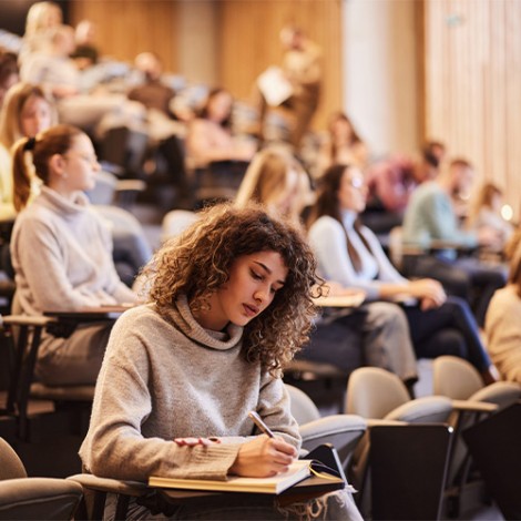 Female college student writing an exam during a class at lecture hall.