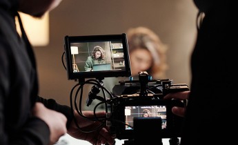 Close-up of steadicam screens with female model using laptop by table