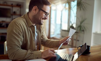 Young happy man analyzing his bills while paying them over laptop at home