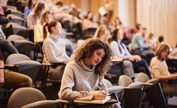 Female college student writing an exam during a class at lecture hall.
